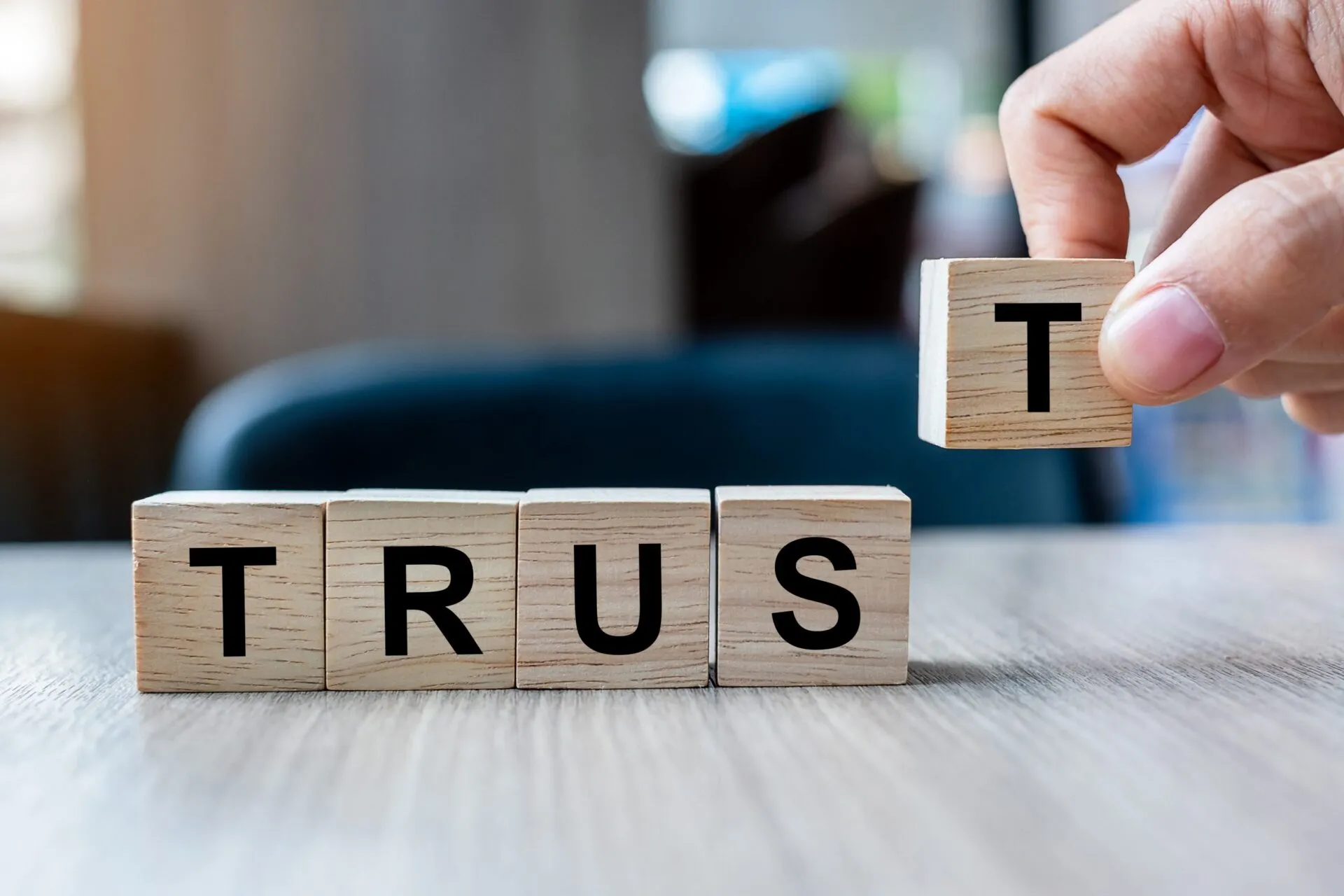Hand placing wooden letter block to complete the word TRUST, symbolizing trust building in legal settings.